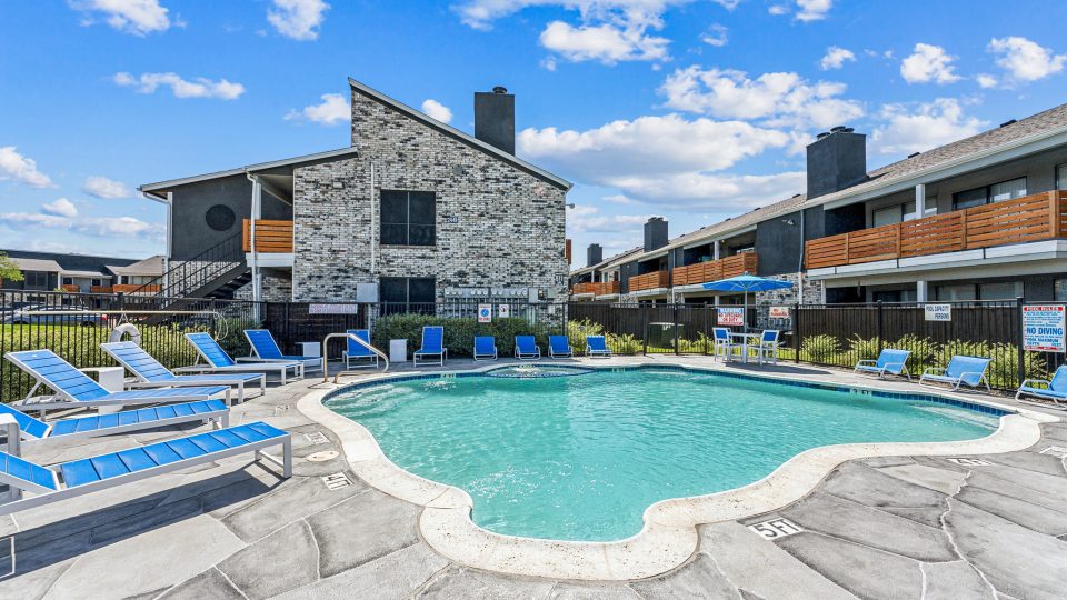 a beach with a pool, chairs, and tables